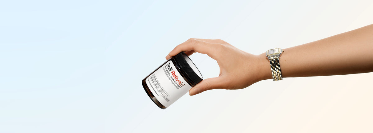 A hand holding a jar of Trelli Relivaid against a soft blue and cream gradient