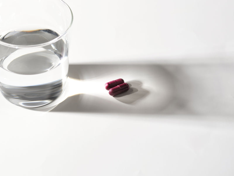 Two Relivaid capsules beside a glass of water