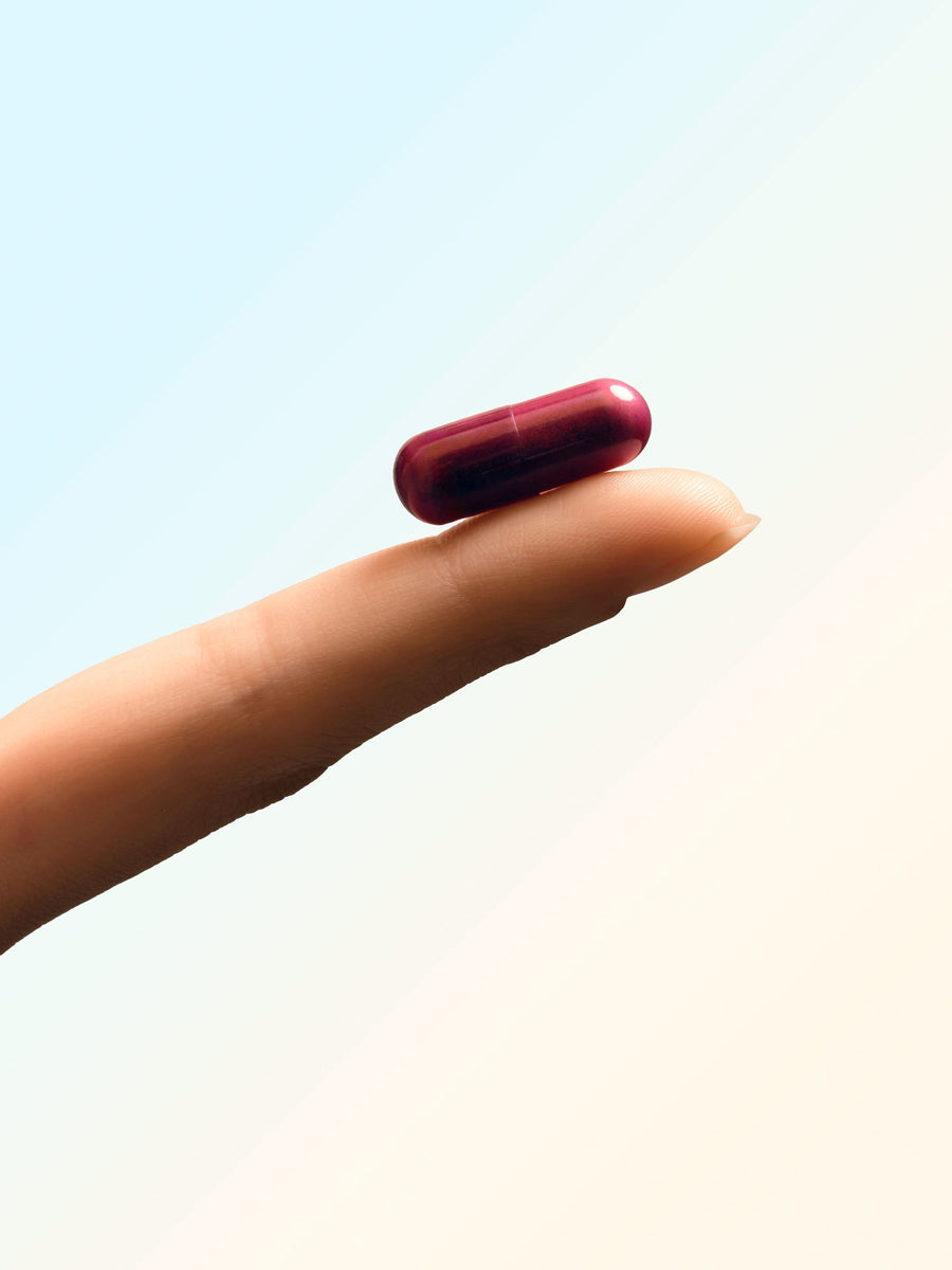 A single maroon Relivaid capsule balanced on a fingertip